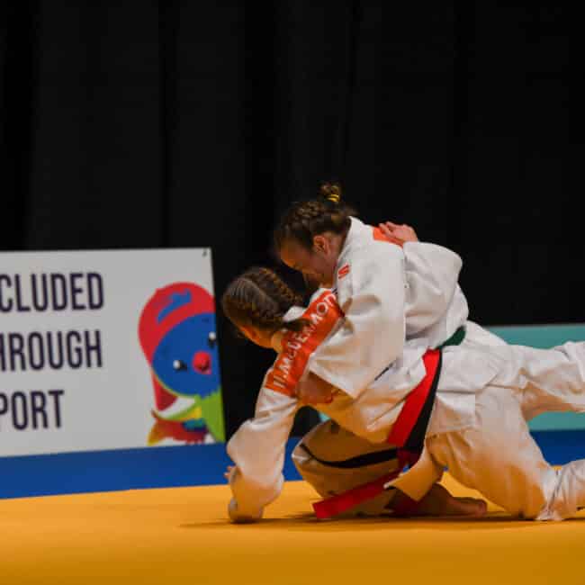 Two female judo athletes in white judogi competing and throwing each other to the ground.