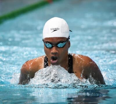 Close-up of female swimmer in a white cap competing in breaststroke in the pool.